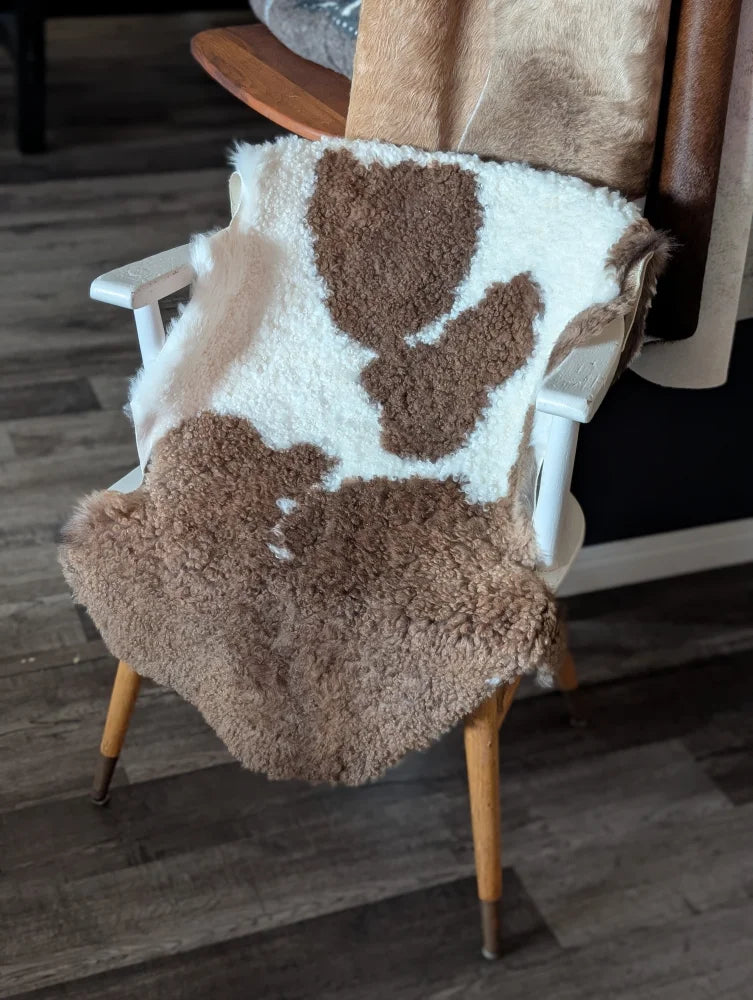 A cozy plush tibet highland spotted sheepskin blanket in natural brown and white draped over a wooden chair