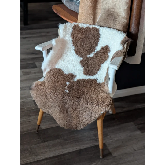 A cozy plush tibet highland spotted sheepskin blanket in natural brown and white draped over a wooden chair