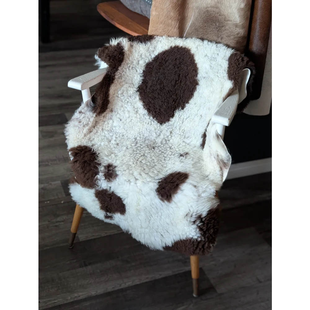 A plush white and brown highland spotted sheepskin throw draped over a white wooden chair