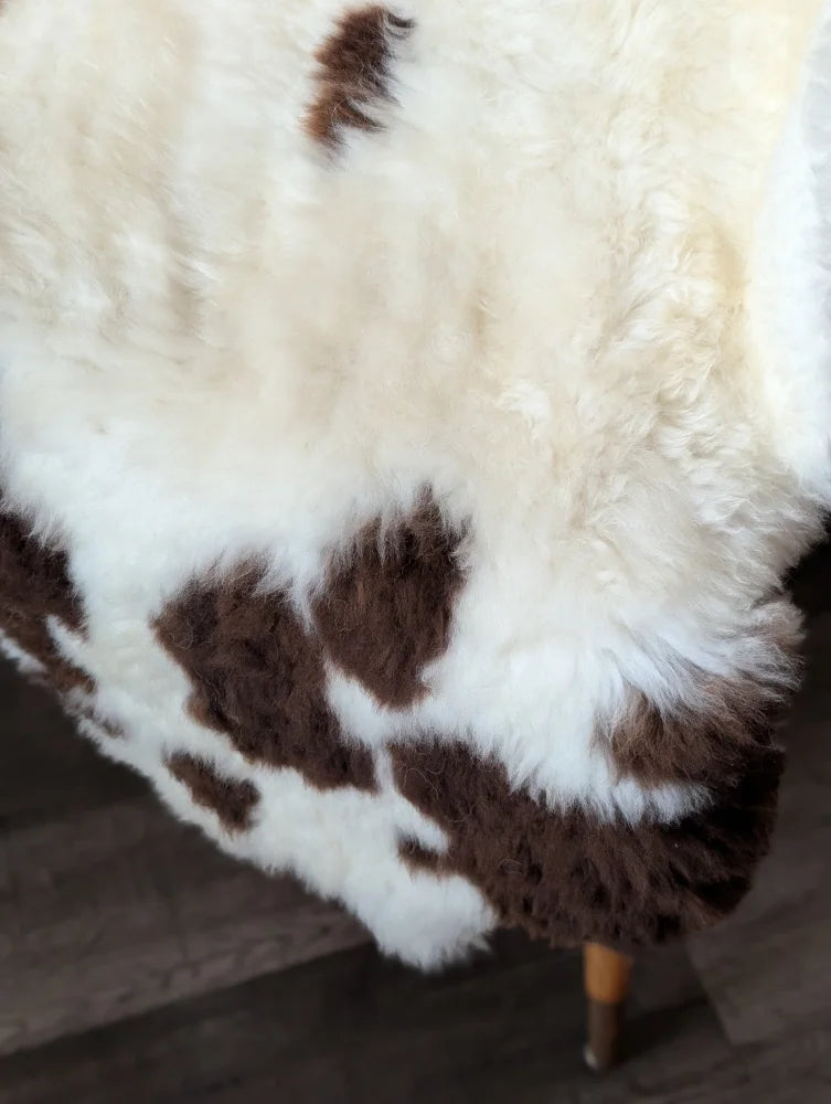 A plush white and brown tibet highland spotted sheepskin rug with soft fluffy texture measuring 43 by 27 inches