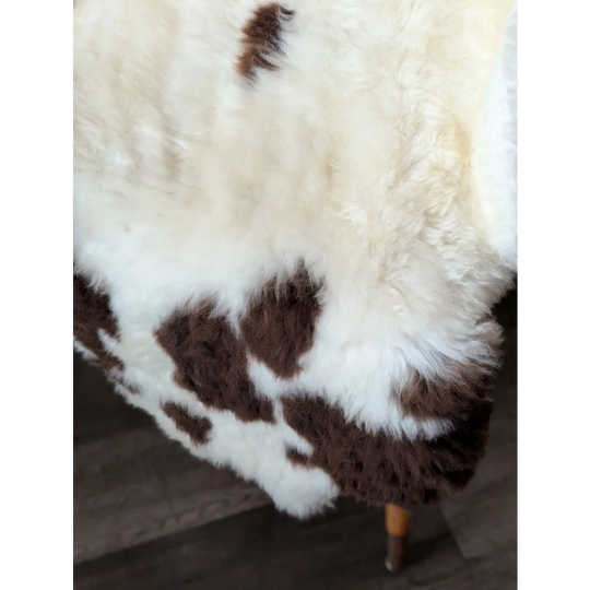 A plush white and brown tibet highland spotted sheepskin rug with soft fluffy texture measuring 43 by 27 inches