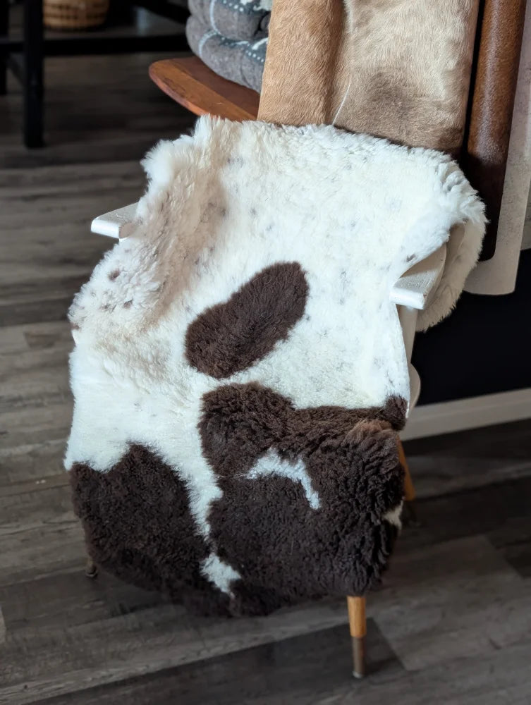A plush tibet highland spotted sheepskin throw blanket in white and brown draped over a wooden chair back