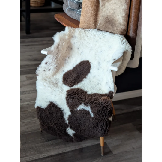 A plush tibet highland spotted sheepskin throw blanket in white and brown draped over a wooden chair back