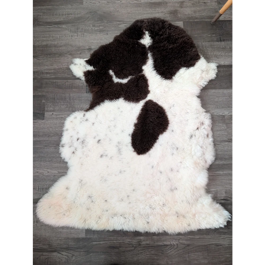 A plush irregular highland spotted sheepskin rug in natural white with bold dark brown patches from tibet highland
