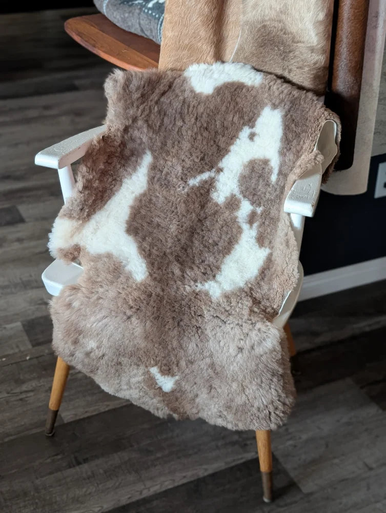 A plush brown and white tibet highland spotted sheepskin rug draped over a wooden chair for cozy decor