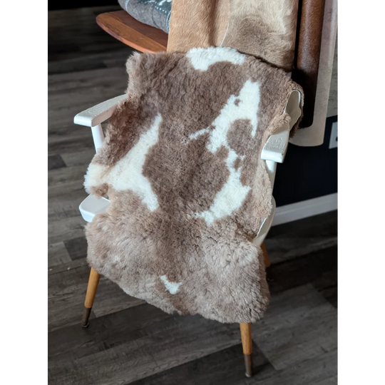 A plush brown and white tibet highland spotted sheepskin rug draped over a wooden chair for cozy decor