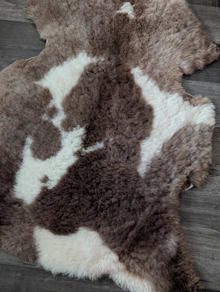 A plush 41.5 x 26 inch tibet highland spotted sheepskin rug with brown and white natural wool pattern grade a