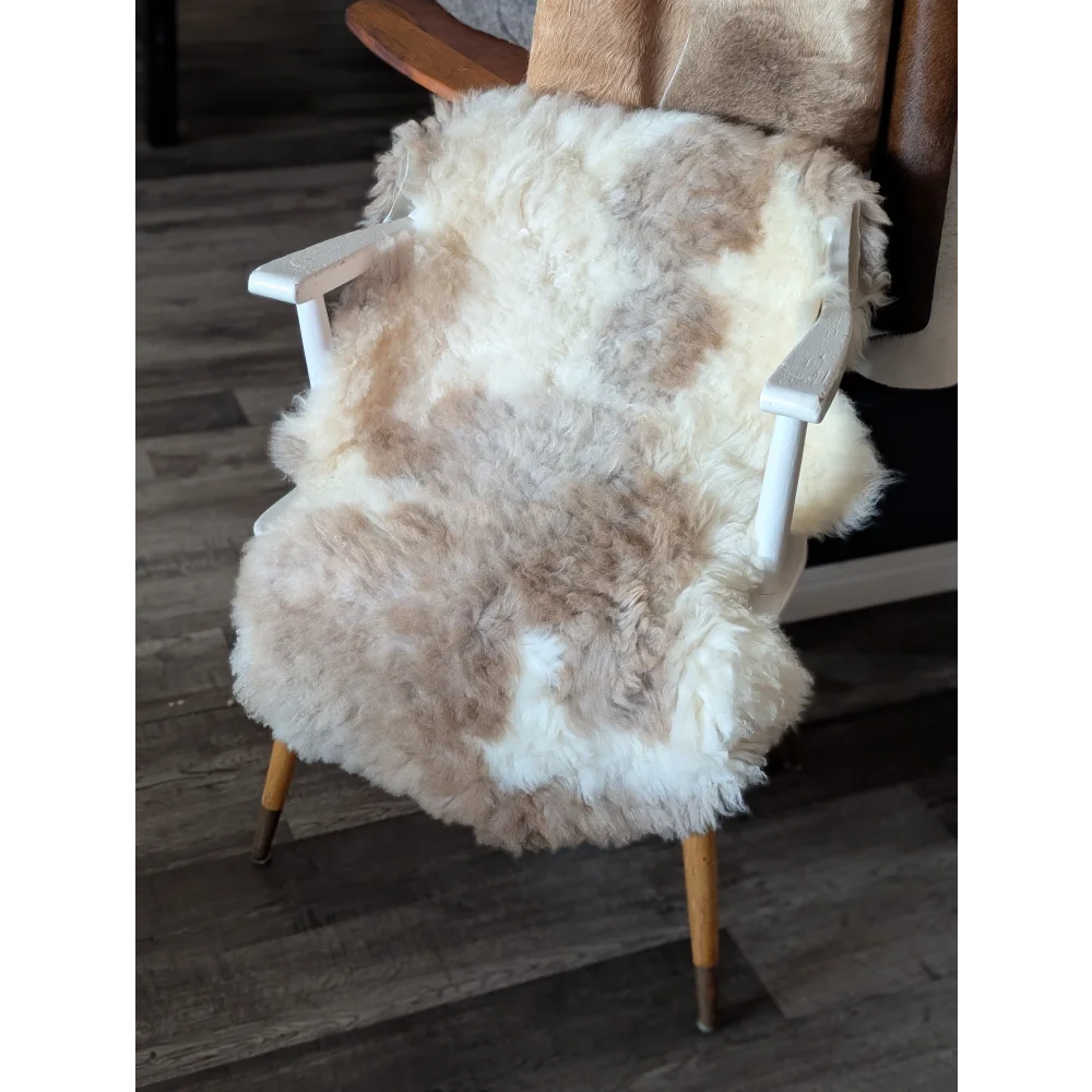 A cozy tibet highland spotted sheepskin chair cover in natural white and beige draped over a mid-century armchair