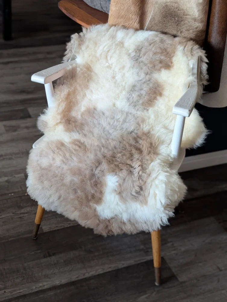 A cozy tibet highland spotted sheepskin chair cover in natural white and beige draped over a mid-century armchair