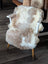 A cozy tibet highland spotted sheepskin chair cover in natural white and beige draped over a mid-century armchair