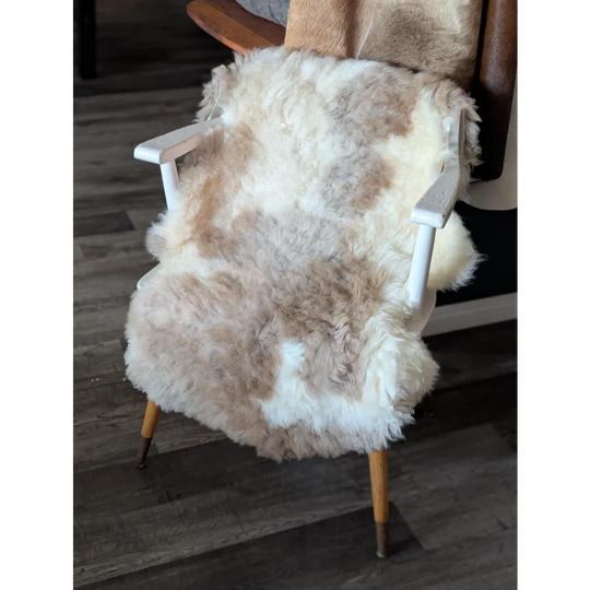 A cozy tibet highland spotted sheepskin chair cover in natural white and beige draped over a mid-century armchair