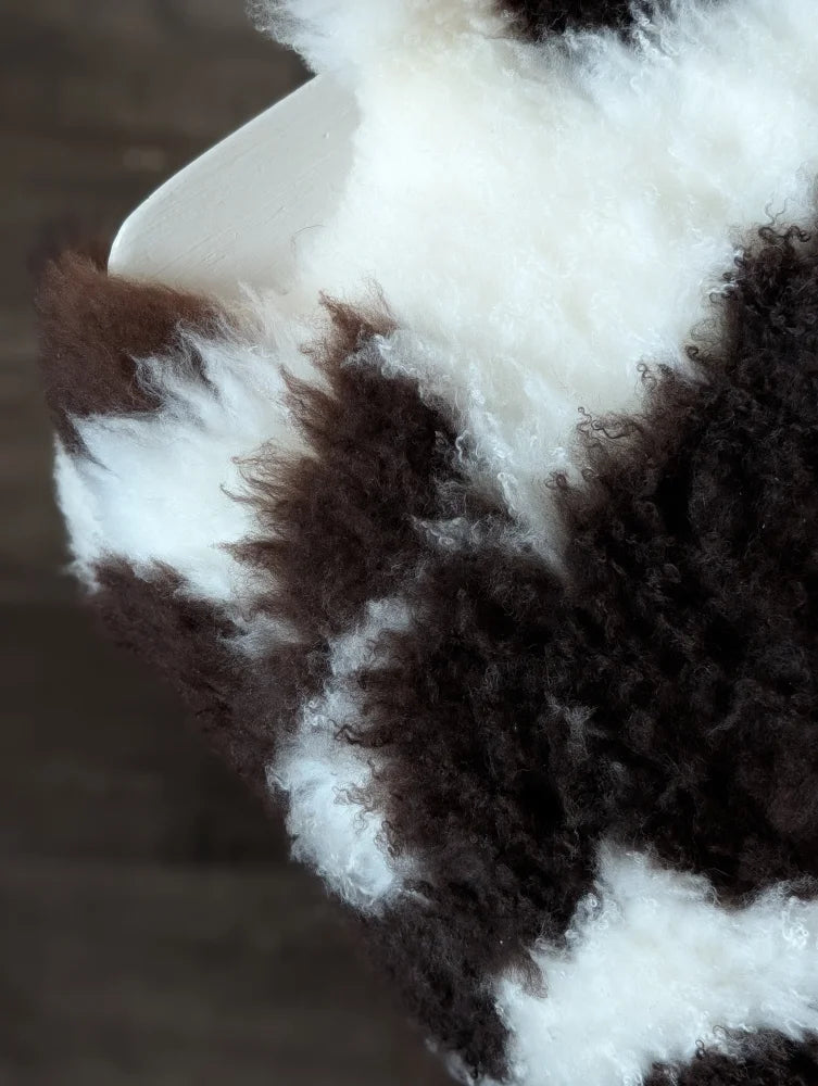 A plush curly brown and white tibet highland spotted sheepskin blanket with soft fluffy texture 39 x 25 inches