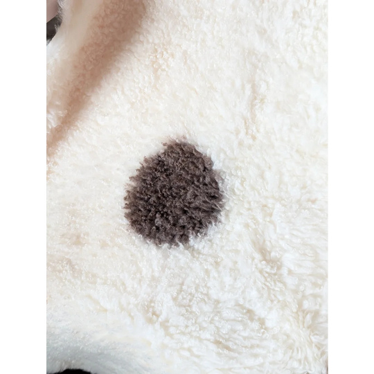 A fluffy dark brown circular patch on a white textured tibet highland spotted sheepskin grade a rug