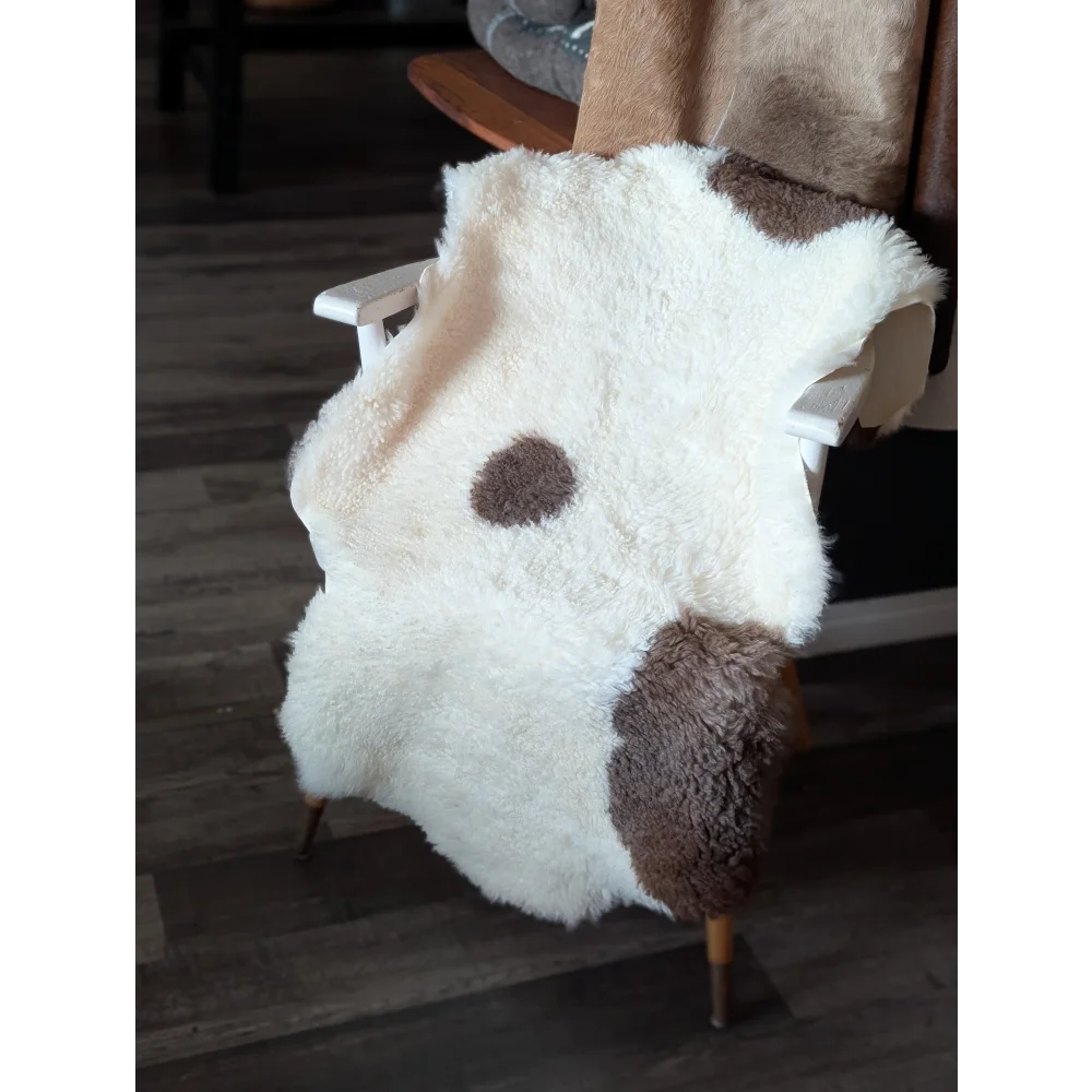 A plush white and brown highland spotted tibet highland spotted sheepskin rug draped over a wooden chair