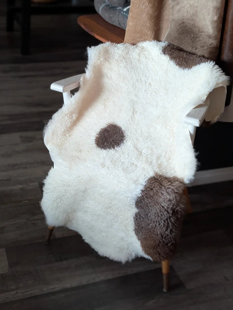 A plush white and brown highland spotted tibet highland spotted sheepskin rug draped over a wooden chair