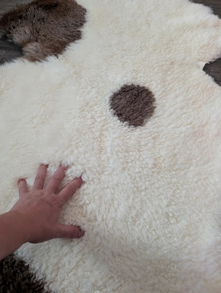 A plush white and brown tibet highland spotted sheepskin rug shaped like a dog perfect for cozy decor
