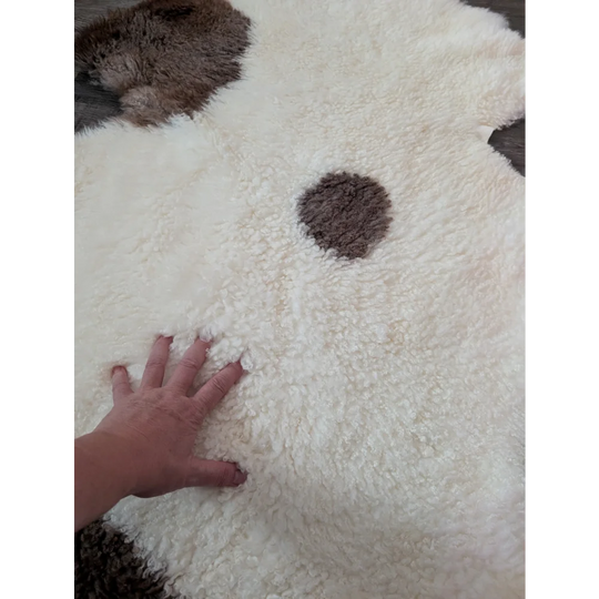 A plush white and brown tibet highland spotted sheepskin rug shaped like a dog perfect for cozy decor