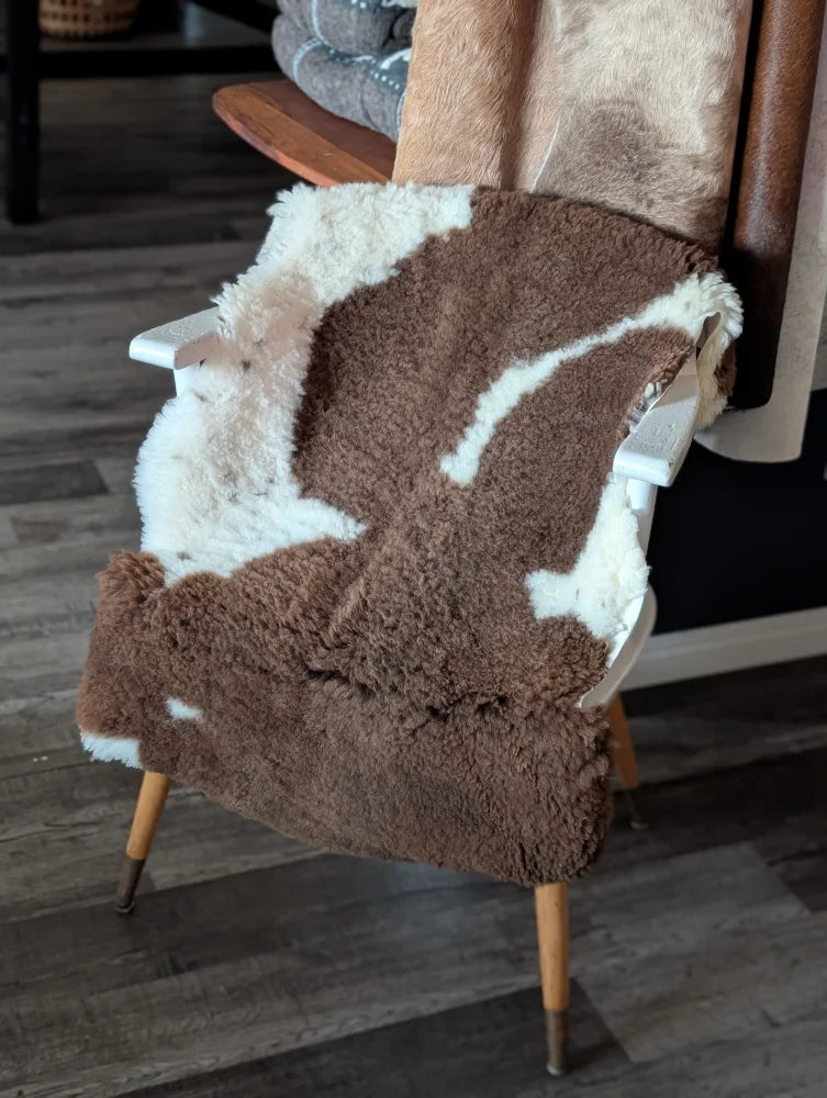 Brown and white tibet highland spotted sheepskin blanket draped over a white wooden chair for cozy use