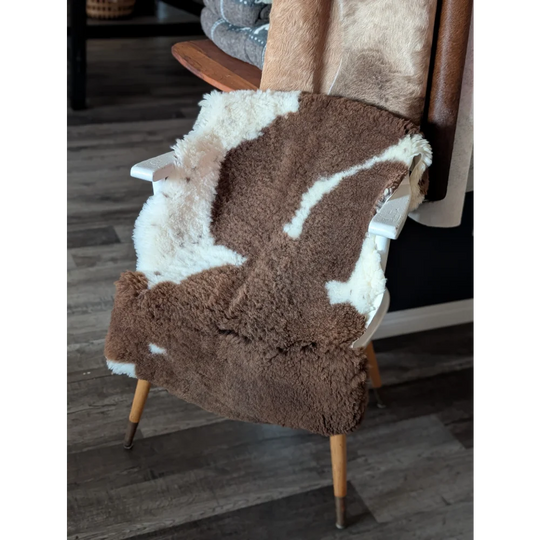 Brown and white tibet highland spotted sheepskin blanket draped over a white wooden chair for cozy use