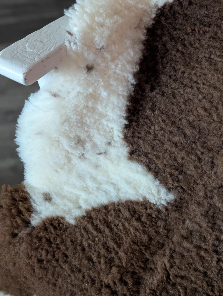 Brown and white fluffy stuffed animal on a 41 x 26 inch gorgeous tibet highland spotted sheepskin grade a rug