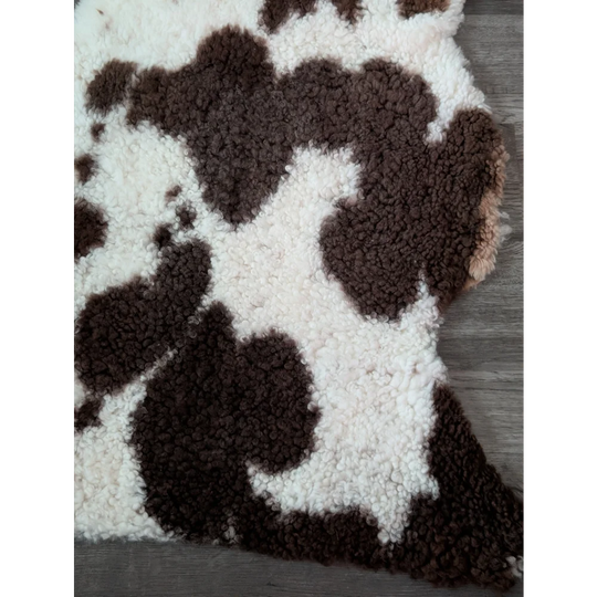A plush tibet highland spotted faux shearling rug in brown and white cow print measuring 41 by 24 inches