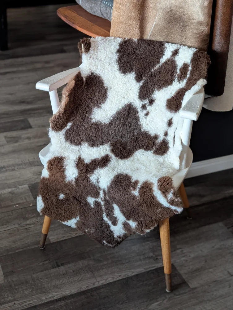 Brown and white tibet highland spotted sheepskin blanket draped over wooden chair measuring 41 by 24 inches