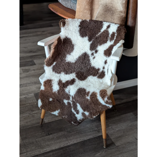 Brown and white tibet highland spotted sheepskin blanket draped over wooden chair measuring 41 by 24 inches