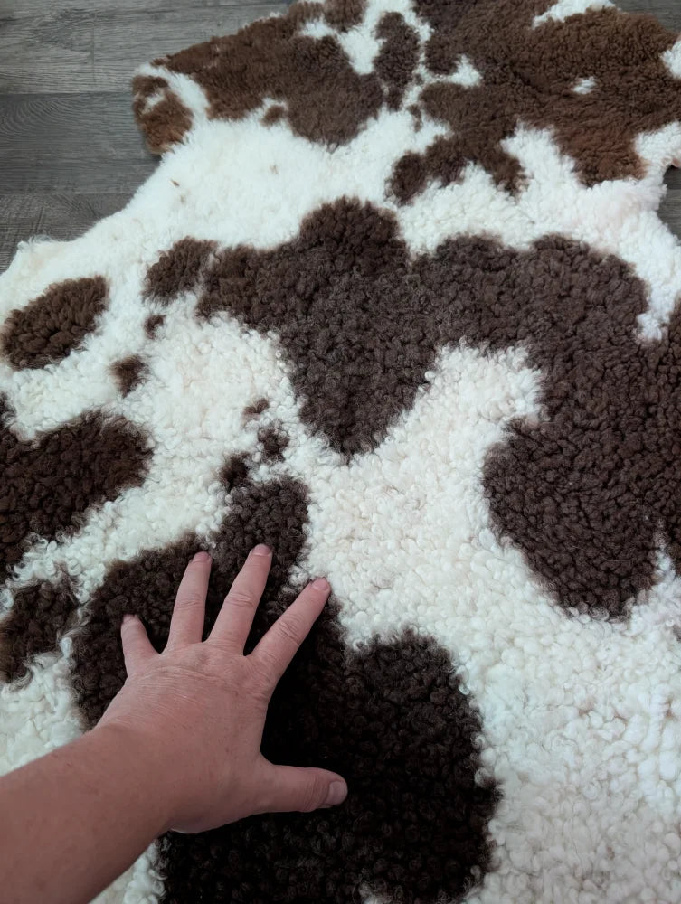 A plush brown and white tibet highland spotted sheepskin rug with a soft textured surface measuring 41 x 24 inches