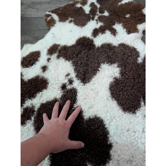 A plush brown and white tibet highland spotted sheepskin rug with a soft textured surface measuring 41 x 24 inches