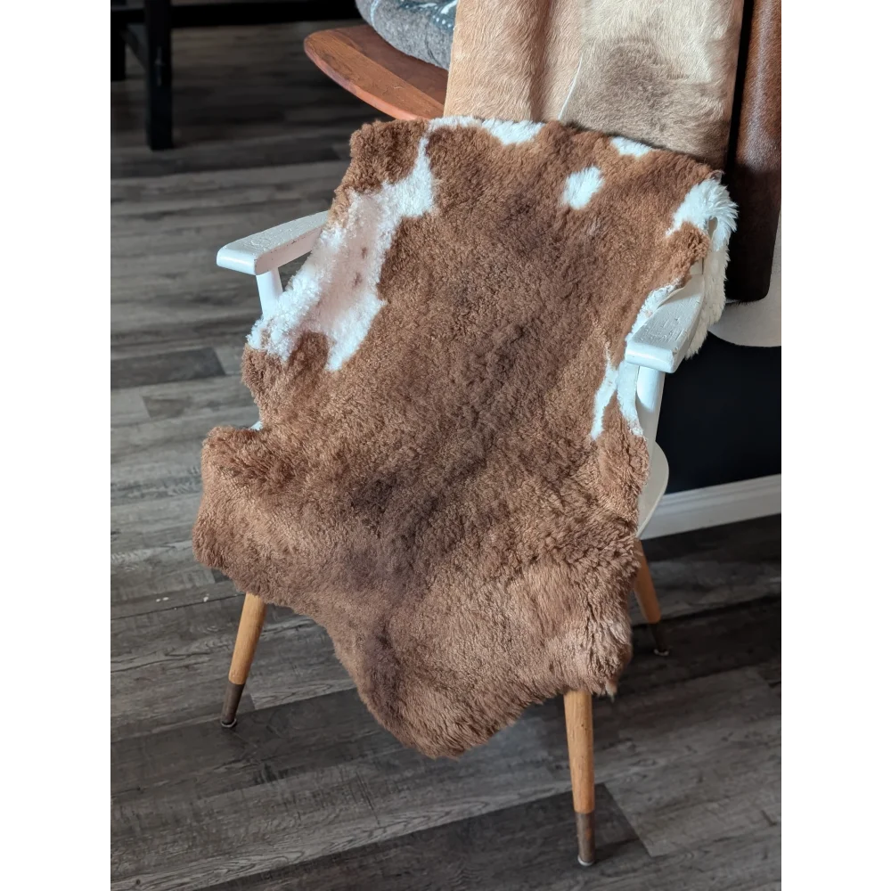 Brown and white tibet highland spotted sheepskin rug draped over wooden chair showcasing soft texture