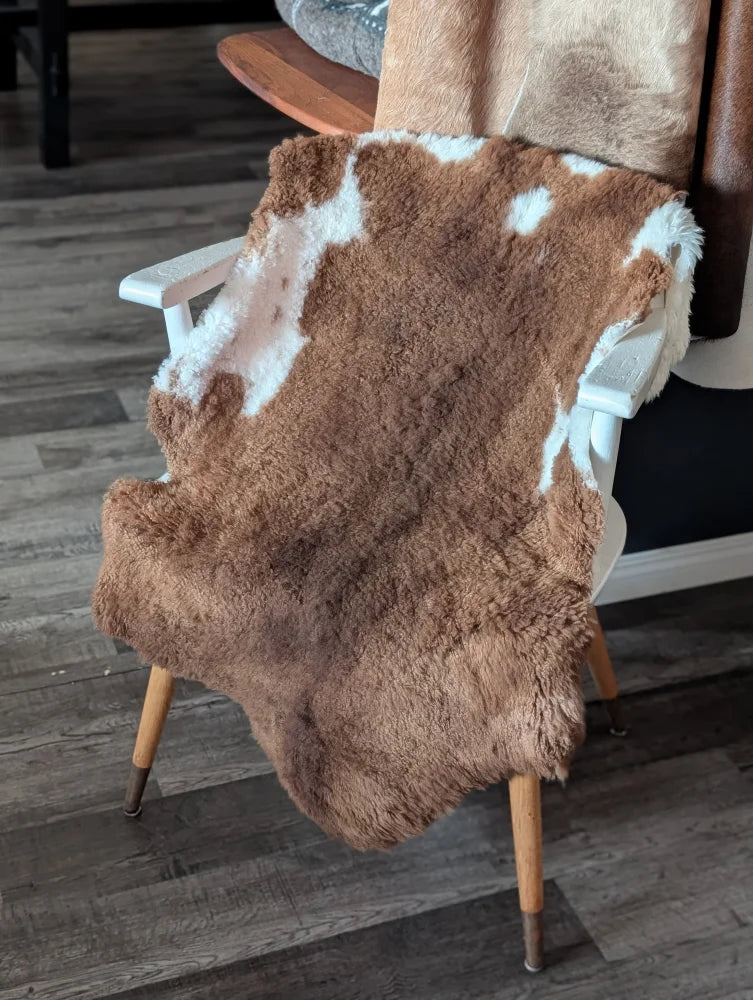 Brown and white tibet highland spotted sheepskin rug draped over wooden chair showcasing soft texture