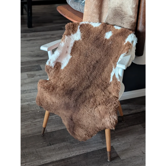 Brown and white tibet highland spotted sheepskin rug draped over wooden chair showcasing soft texture