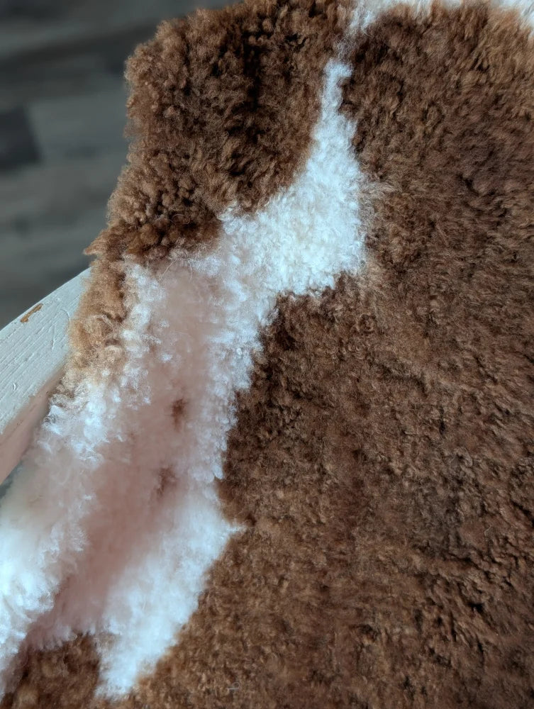 A plush fluffy brown and white tibet highland spotted sheepskin fabric with a soft textured surface for decor