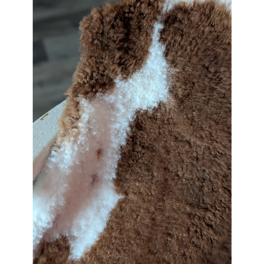 A plush fluffy brown and white tibet highland spotted sheepskin fabric with a soft textured surface for decor
