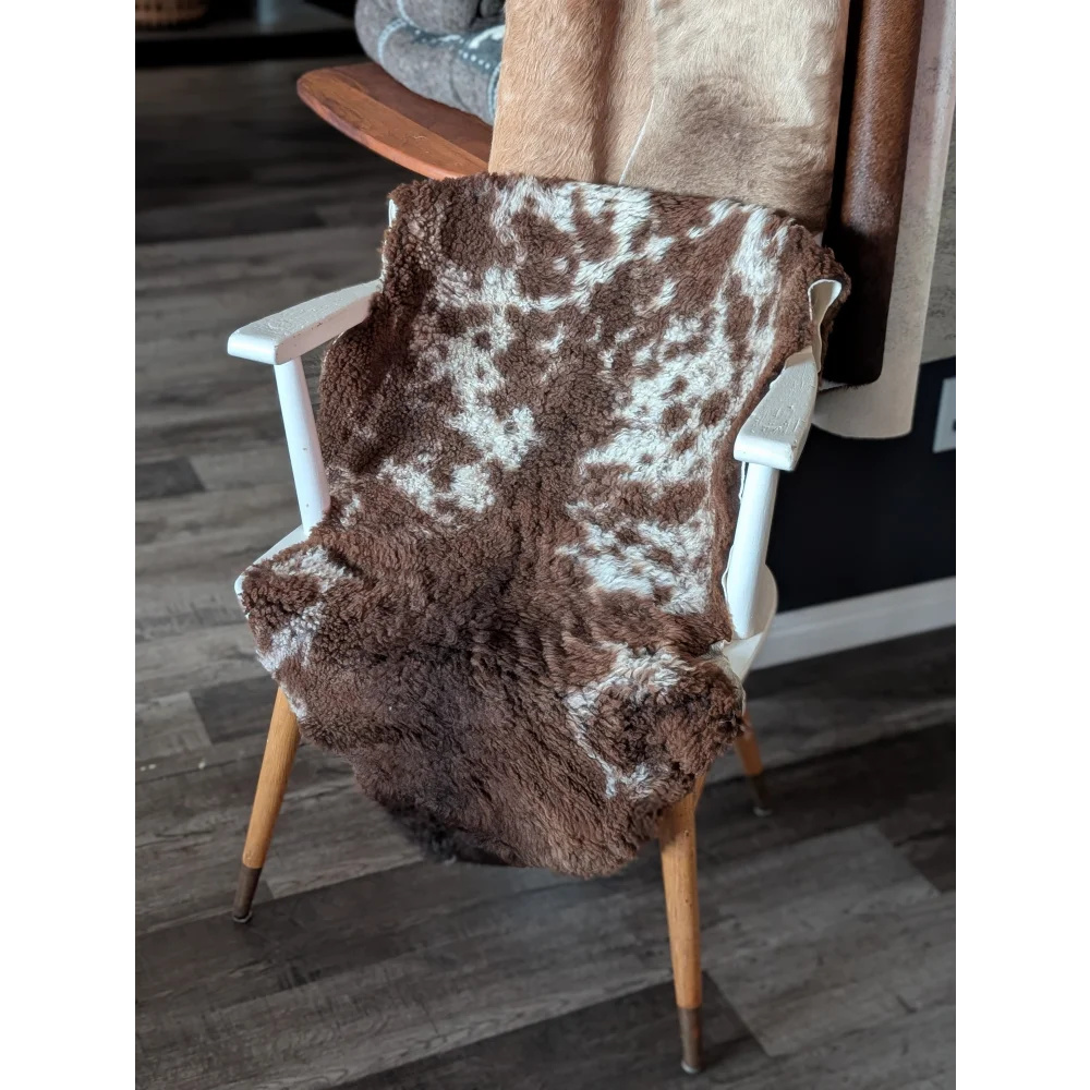 Brown and white tibet highland spotted sheepskin blanket draped over a white wooden chair for cozy decor