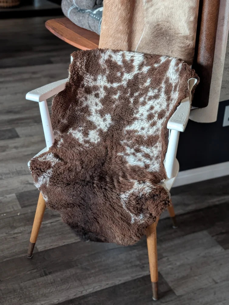 Brown and white tibet highland spotted sheepskin blanket draped over a white wooden chair for cozy decor