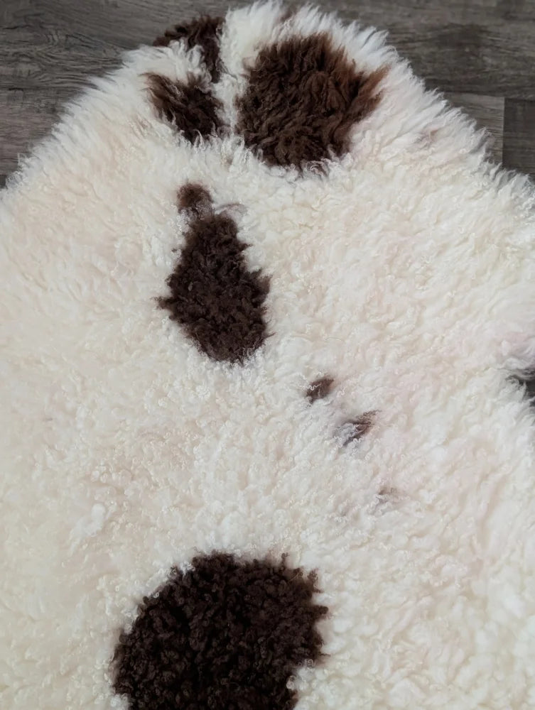 A plush white and brown paw print rug made from soft tibet highland spotted sheepskin grade a material