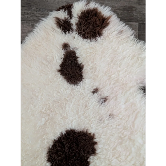 A plush white and brown paw print rug made from soft tibet highland spotted sheepskin grade a material