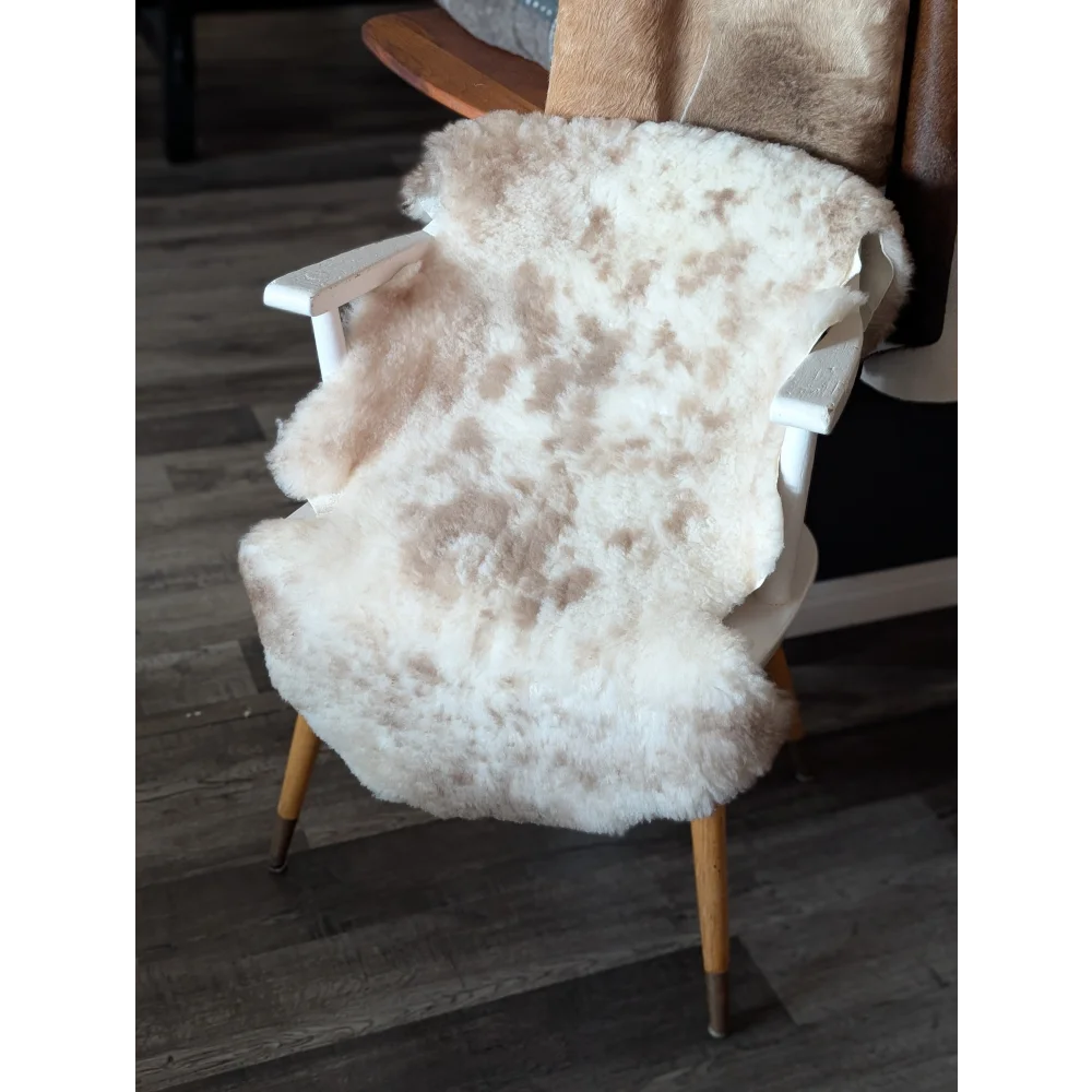 A plush cream-colored tibet highland spotted sheepskin rug draped over a white wooden chair with light wood legs