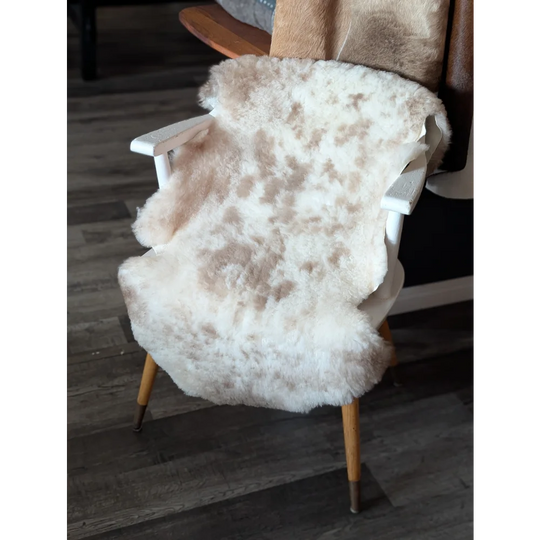 A plush cream-colored tibet highland spotted sheepskin rug draped over a white wooden chair with light wood legs