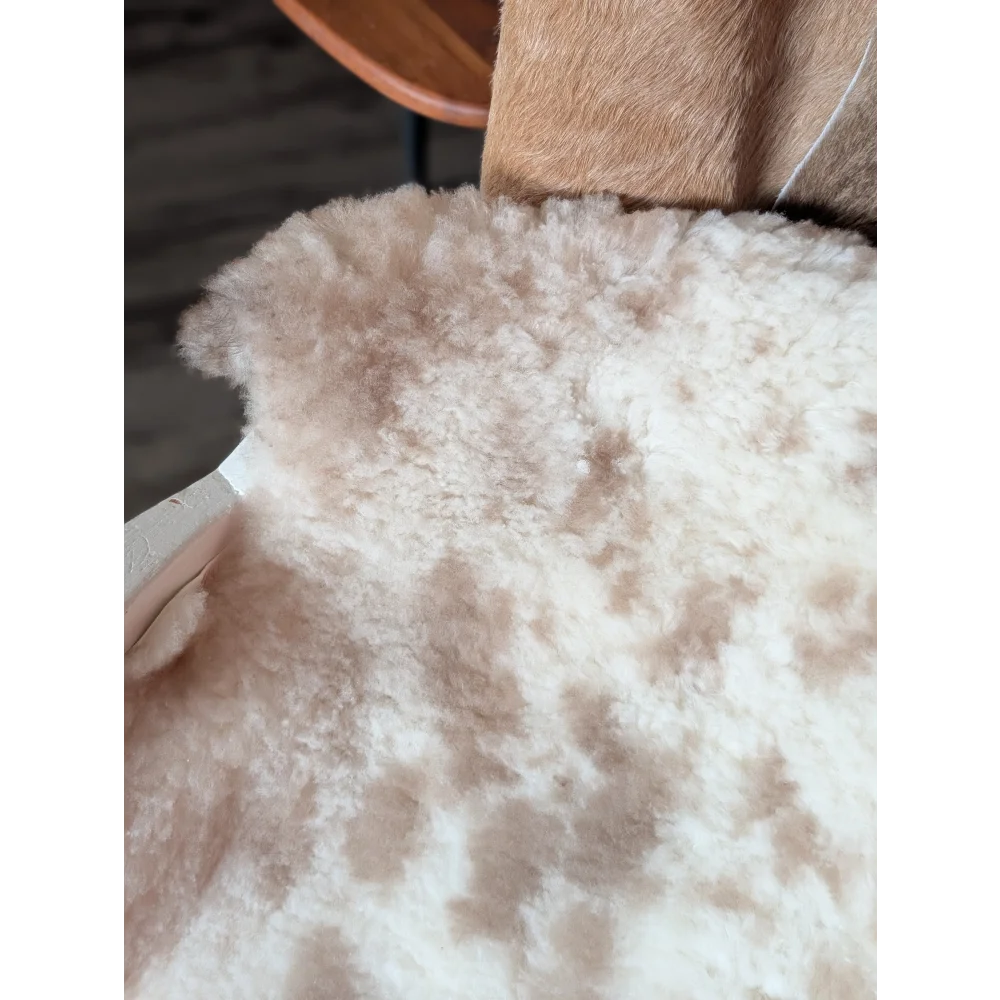 A plush cream-colored tibet highland spotted sheepskin rug with soft fluffy texture and natural tan patches