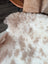A plush cream-colored tibet highland spotted sheepskin rug with soft fluffy texture and natural tan patches