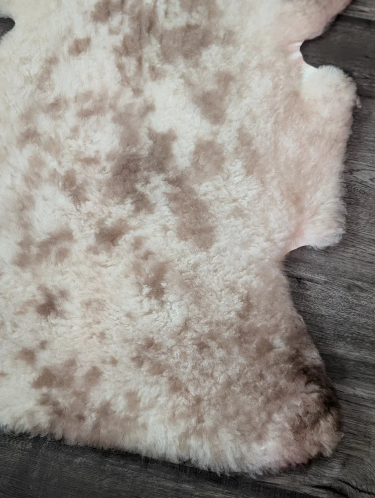 A soft tibet highland spotted sheepskin rug in creamy white and light brown with a natural mottled pattern
