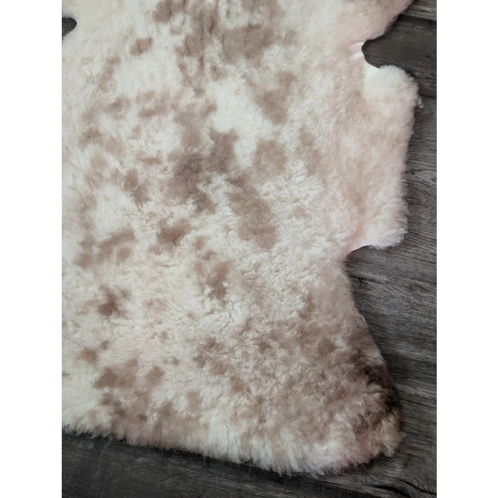 A soft tibet highland spotted sheepskin rug in creamy white and light brown with a natural mottled pattern