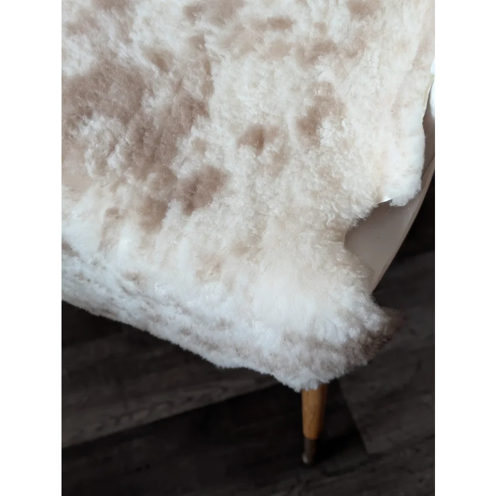 A plush cream-colored tibet highland spotted sheepskin rug with soft fluffy texture and natural brown speckles
