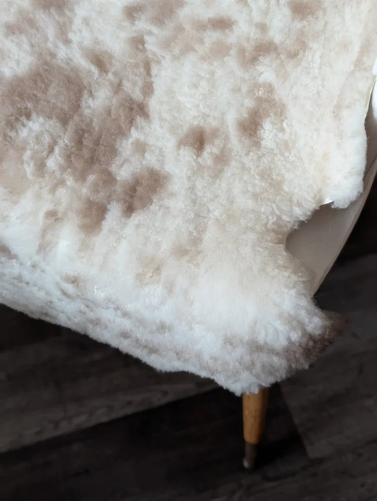 A plush cream-colored tibet highland spotted sheepskin rug with soft fluffy texture and natural brown speckles