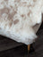 A plush cream-colored tibet highland spotted sheepskin rug with soft fluffy texture and natural brown speckles