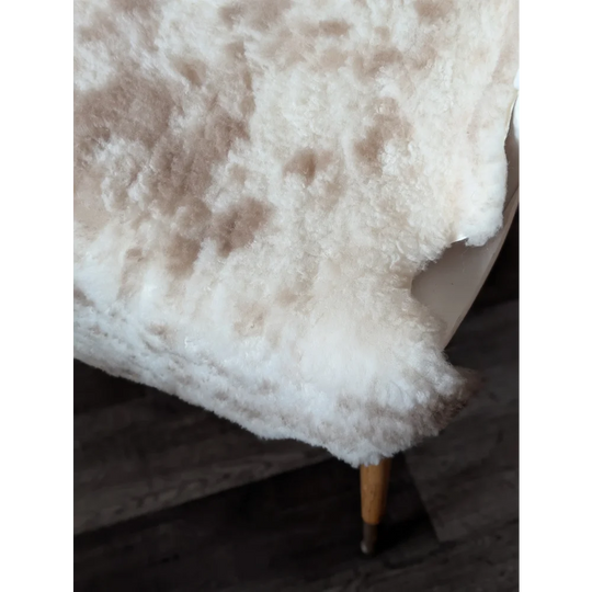 A plush cream-colored tibet highland spotted sheepskin rug with soft fluffy texture and natural brown speckles