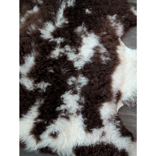 A plush grade a tibet highland spotted sheepskin rug with natural brown and white curly fur measuring 42 x 27 inches