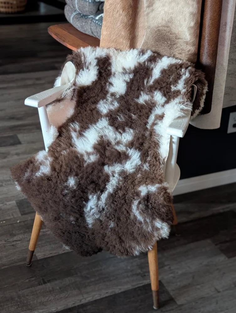 Brown and white tibet highland spotted sheepskin throw draped over a white wooden chair for cozy decor